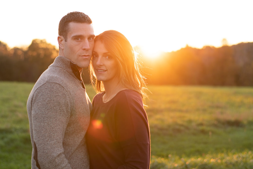 Engaged couple in field at sunset with sun coming in behind them with Sharon Leger Photography