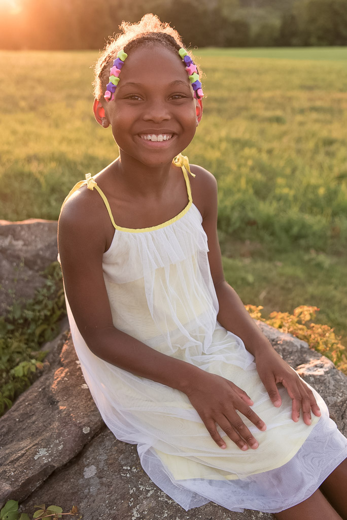 Little girl smiling at camera in field at sunset