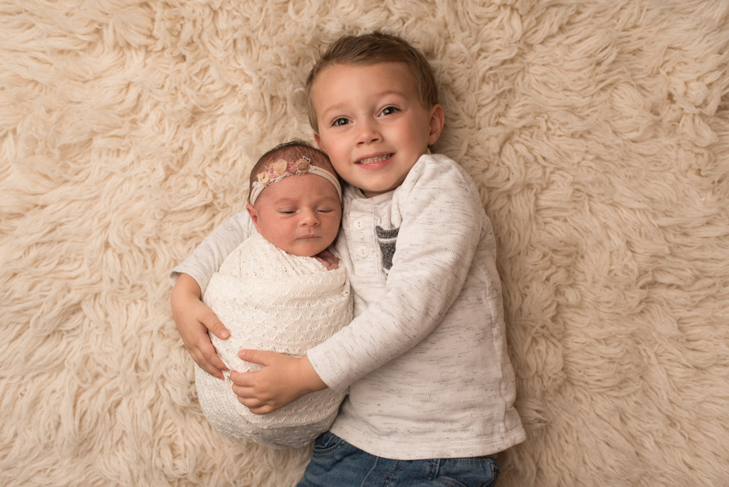 Little brother hugging newborn little sister wrapped in white