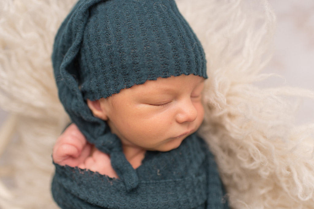 Close up of newborn boy wearing teal hat and wrapped in teal wrap
