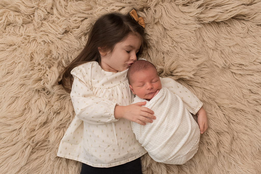 Newborn boy wrapped in white at newborn session with sister