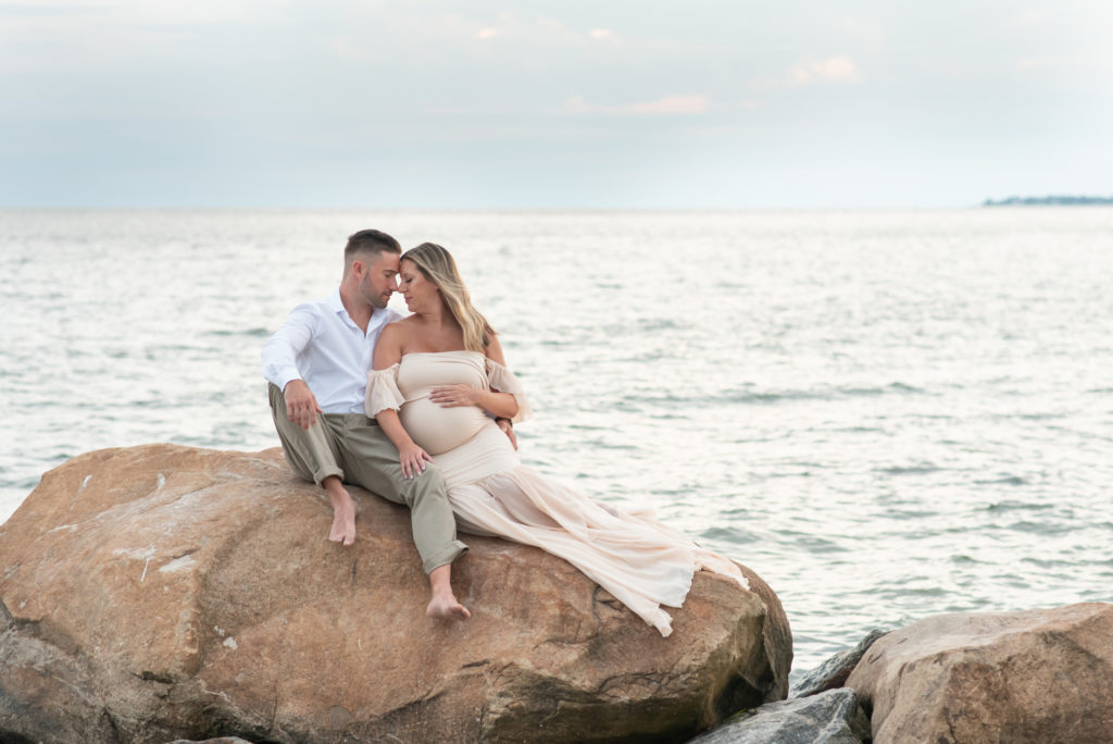 Mother and father sitting on rock at beach maternity session