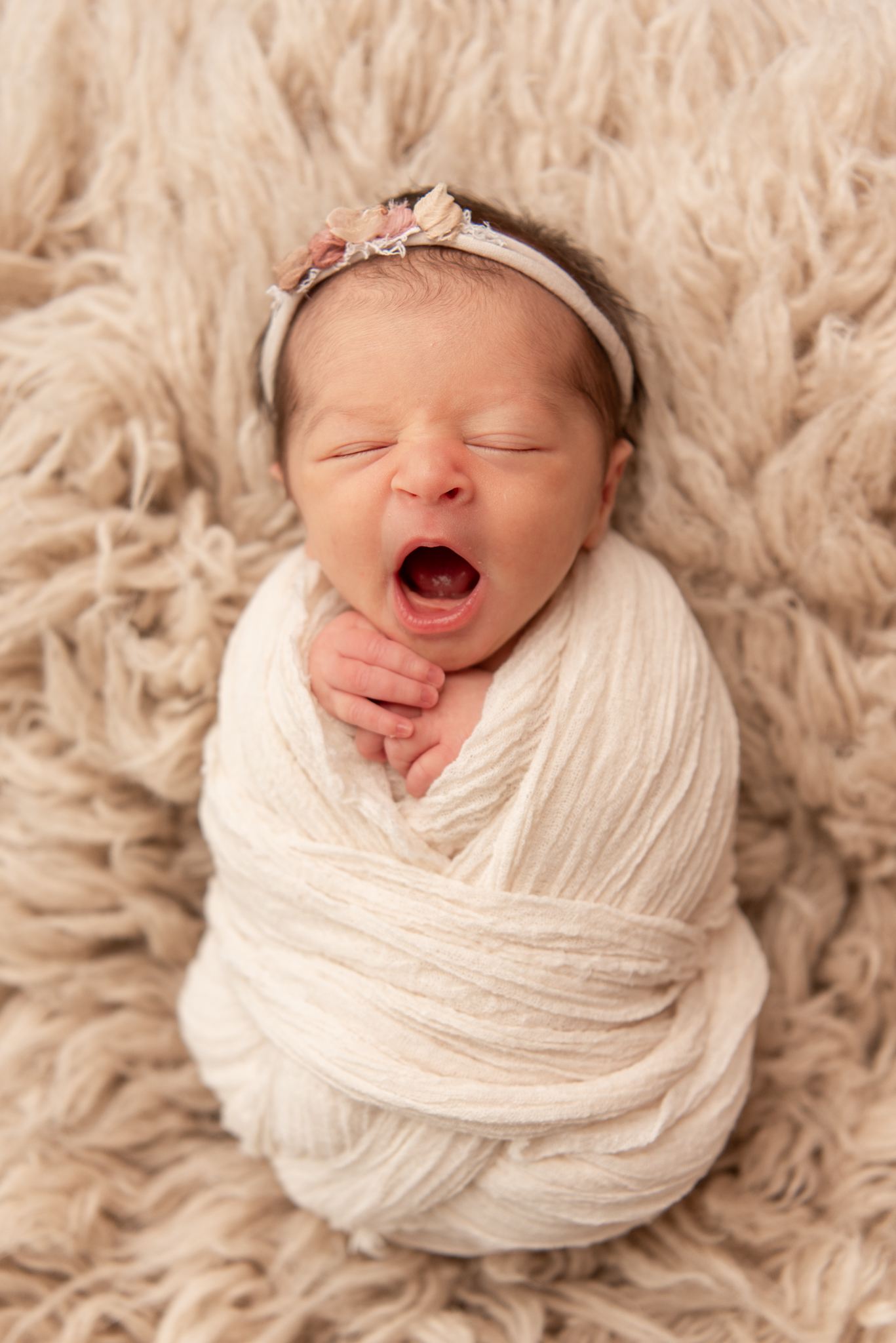 Baby girl swaddled in white, yawning at newborn session