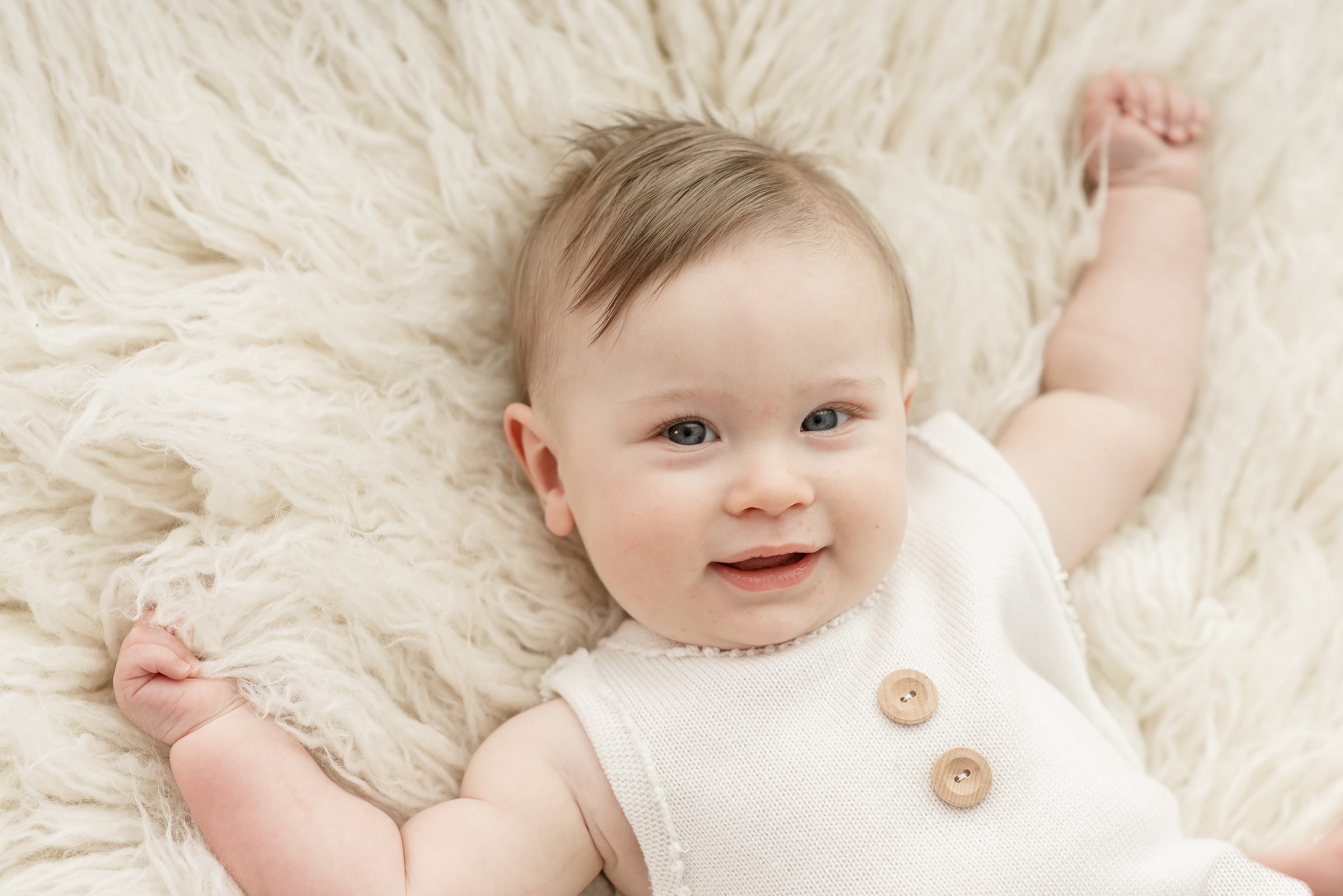 Six month old boy smiling at the camera on a white rug