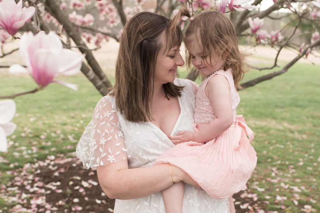 Mother in white dress smiling at her young daughter in a pink dress at their Connecticut spring blossom mini session